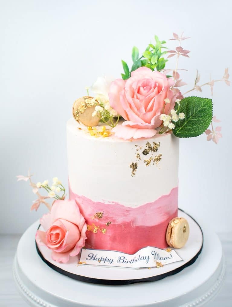 legant pink and white birthday cake with floral decorations and gold accents