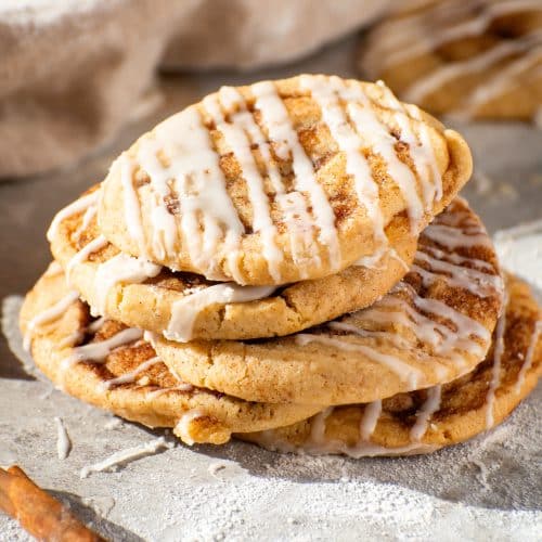 Stack of soft and chewy cinnamon roll cookies drizzled with sweet glaze, showcasing golden-brown edges and cinnamon-sugar swirls.