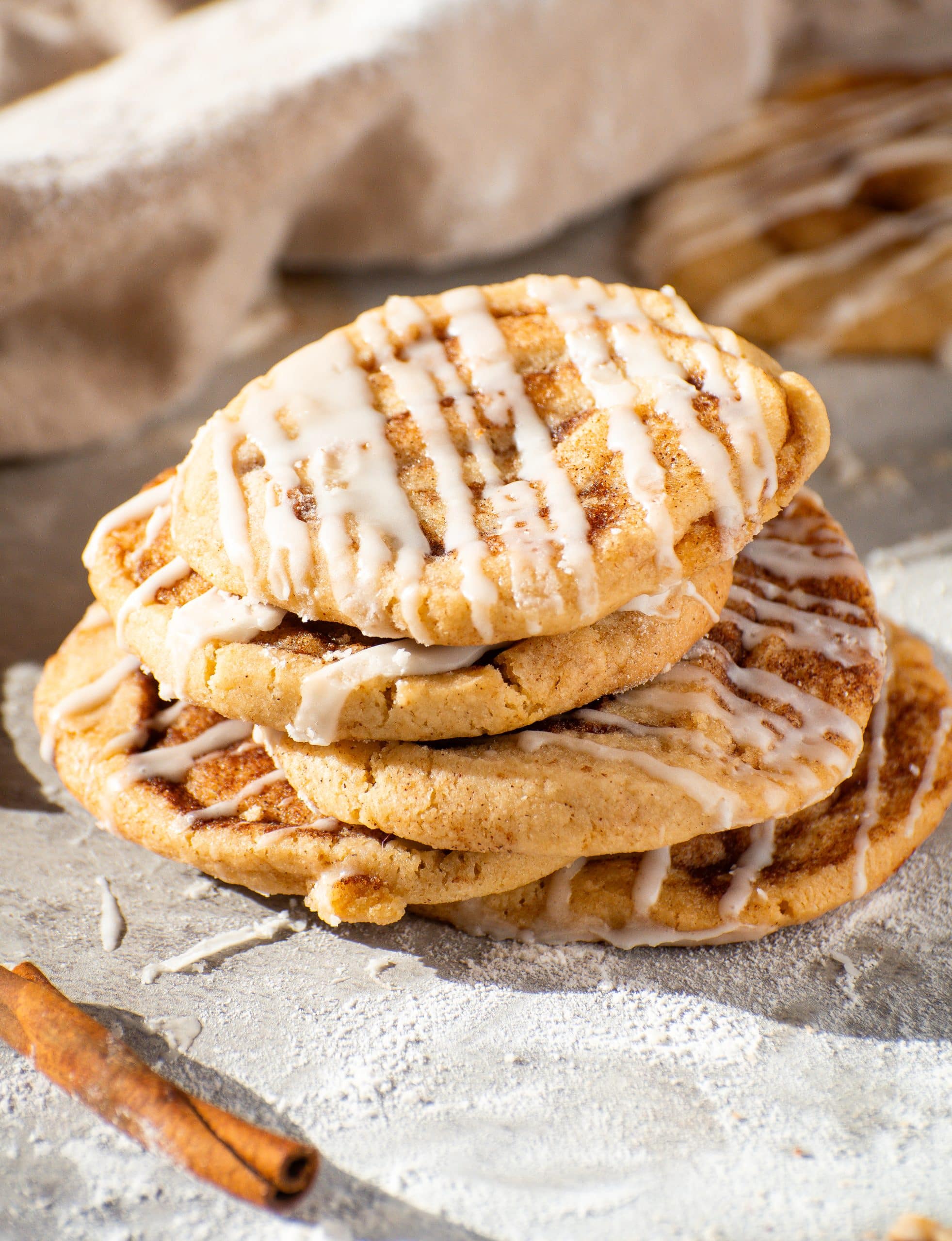 Stack of soft and chewy cinnamon roll cookies drizzled with sweet glaze, showcasing golden-brown edges and cinnamon-sugar swirls.