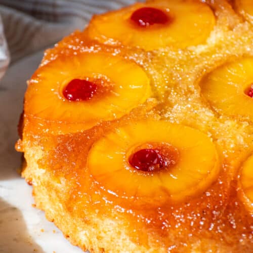 Moist pineapple upside down cake with glossy brown sugar caramel, pineapple rings, and cherries baked on top.