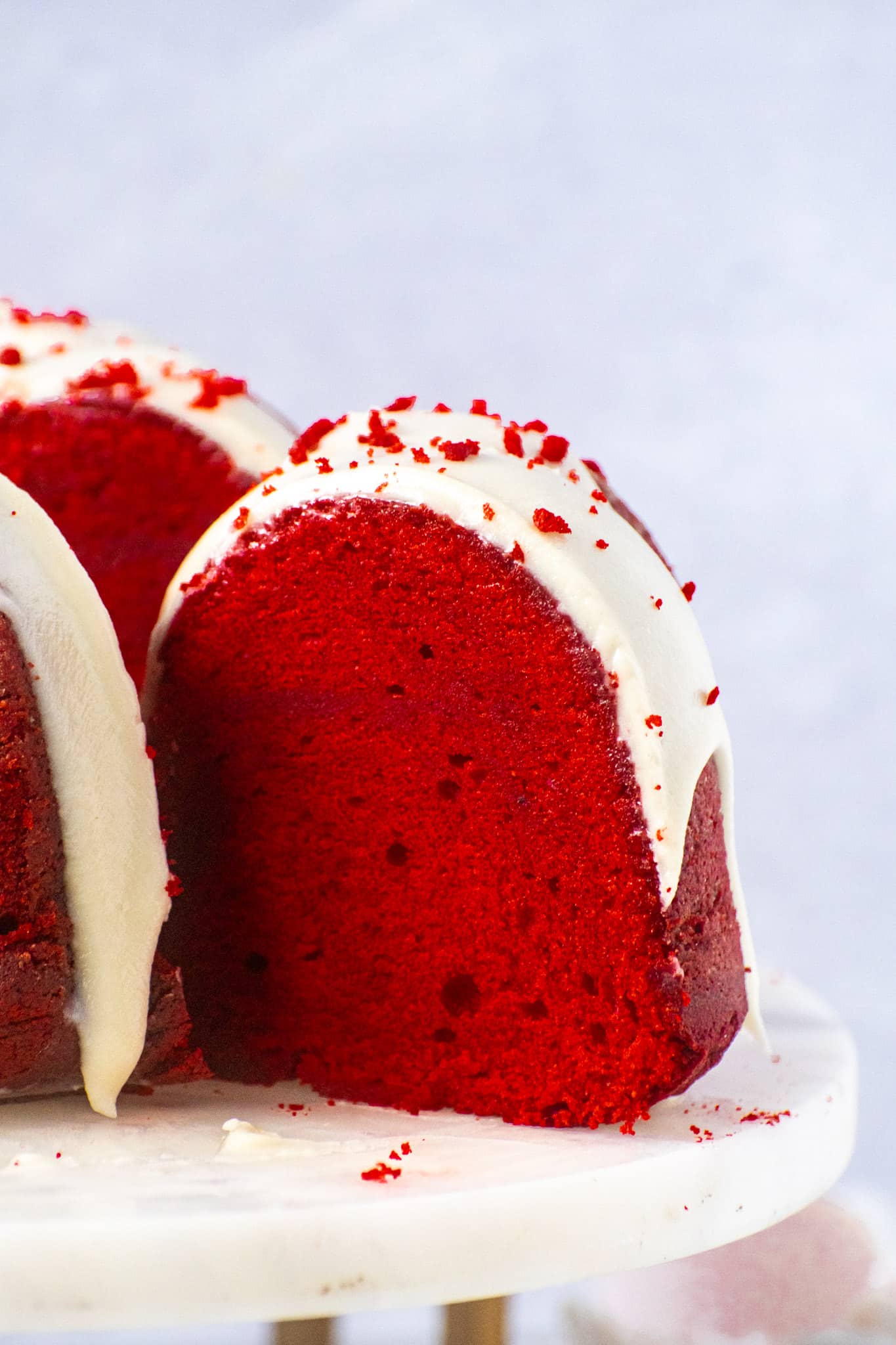 Red velvet pound cake with cream cheese frosting, sliced to show moist red interior and topped with frosting and cake crumbs.