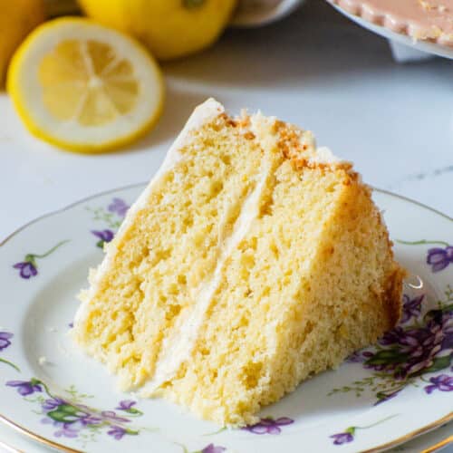 lemon layer cake slice on floral plate with fresh lemons showing soft moist fluffy texture