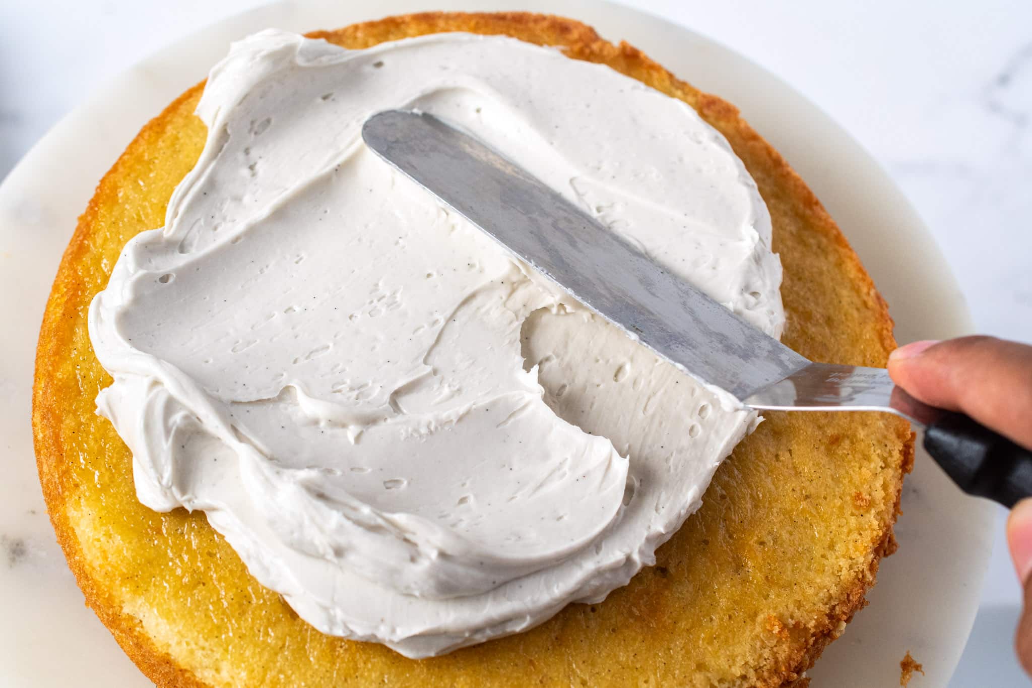 Hand frosting a vanilla cake layer with an offset spatula and fluffy vanilla buttercream.