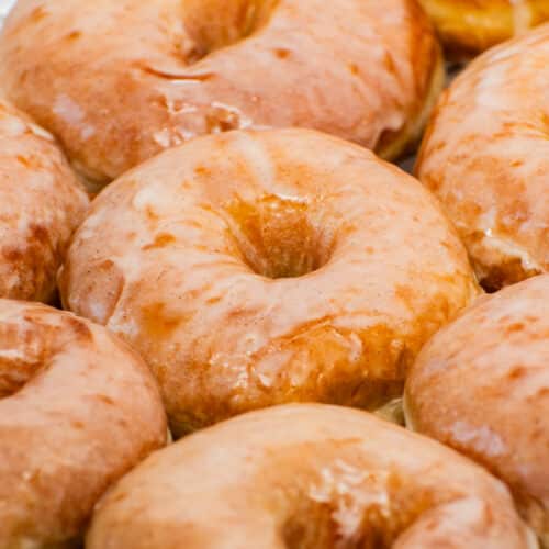 Fresh homemade glazed donuts with shiny vanilla glaze close up, soft fluffy yeast donuts with bakery-style crackly icing
