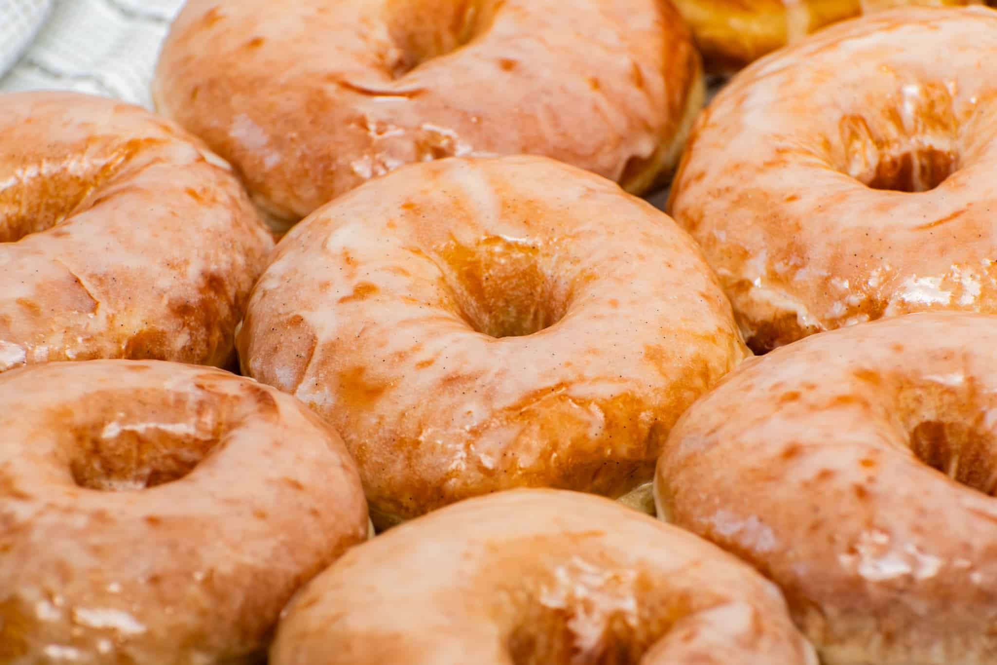Fresh homemade glazed donuts with shiny vanilla glaze close up, soft fluffy yeast donuts with bakery-style crackly icing