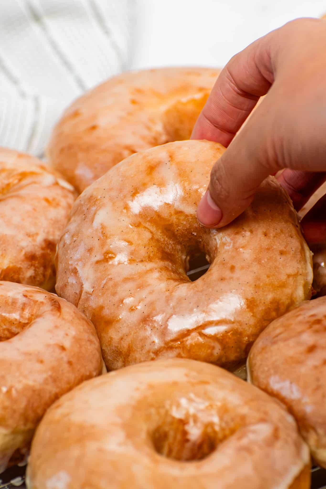 Fresh homemade glazed donuts with glossy vanilla glaze stacked on a cooling rack, soft fluffy yeast donuts better than Krispy Kreme