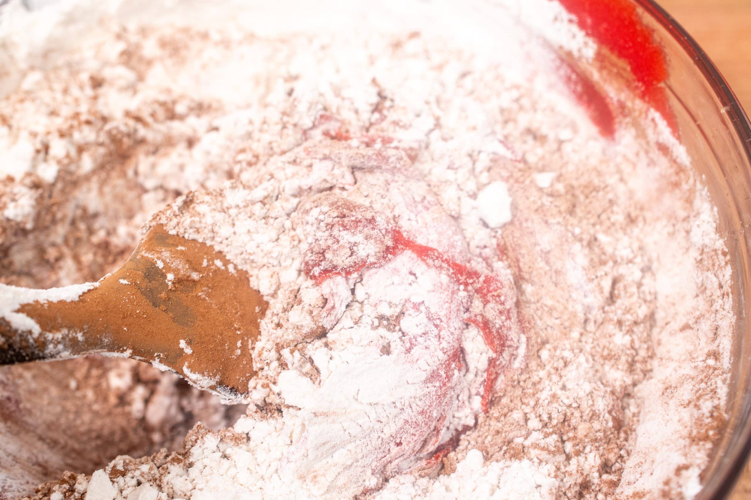 Dry ingredients being incorporated into red velvet cookie dough with a wooden spatula.
