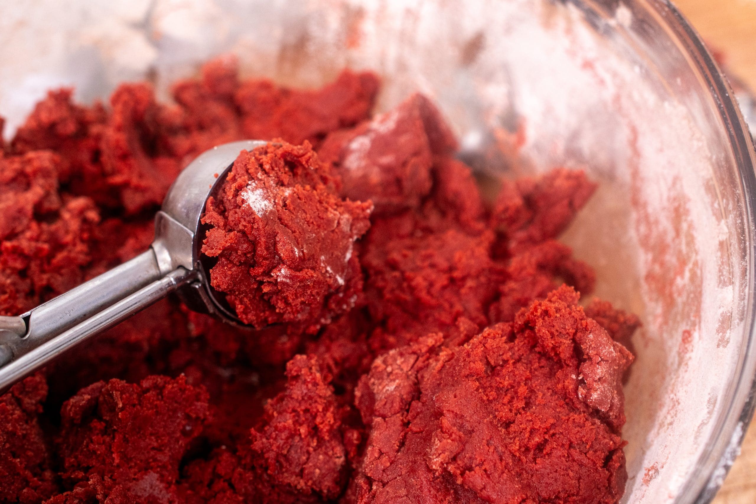 Scooping red velvet cookie dough with a cookie scoop for even portions.