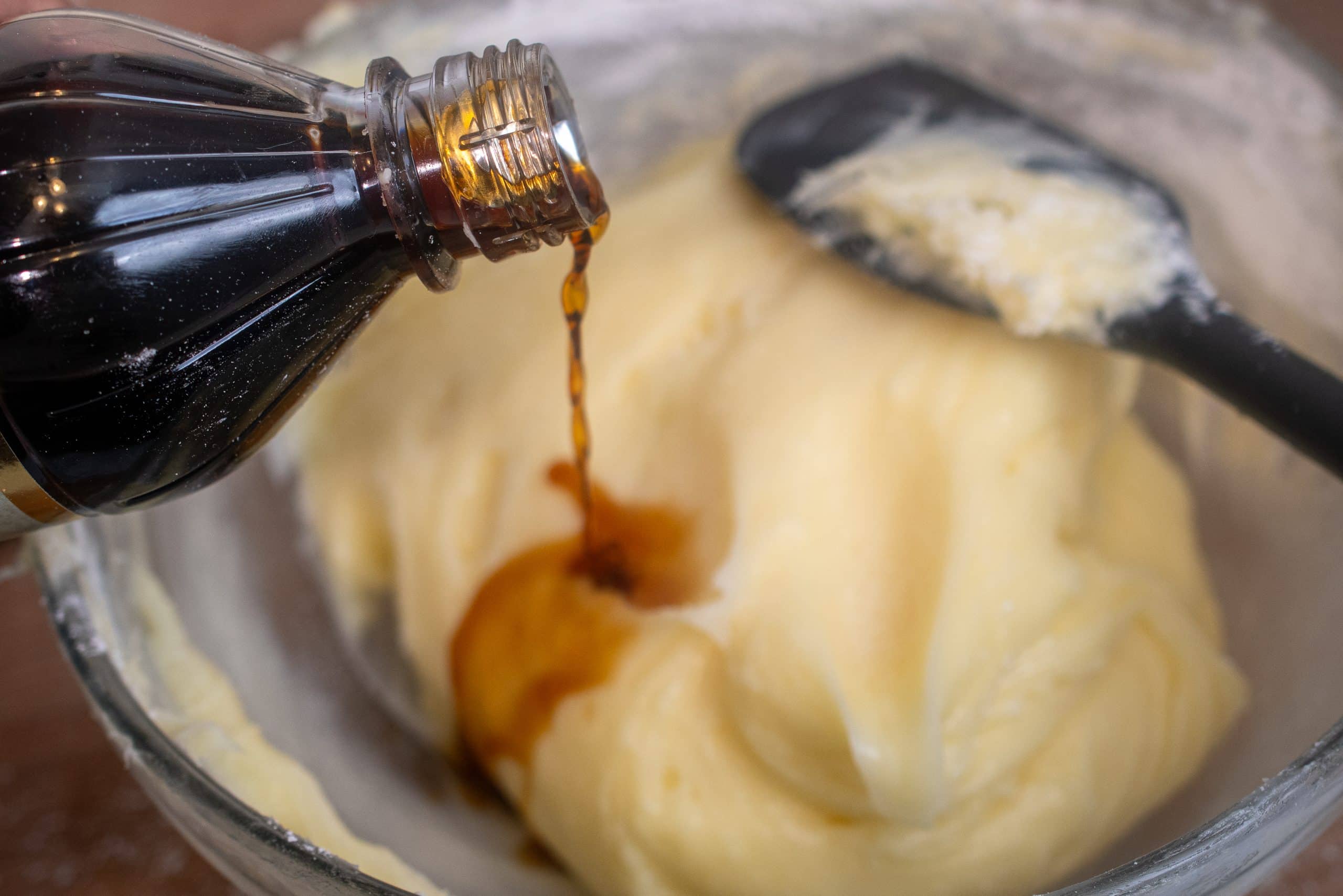 Pouring vanilla extract into a bowl of cream cheese frosting for a rich and flavorful finish.