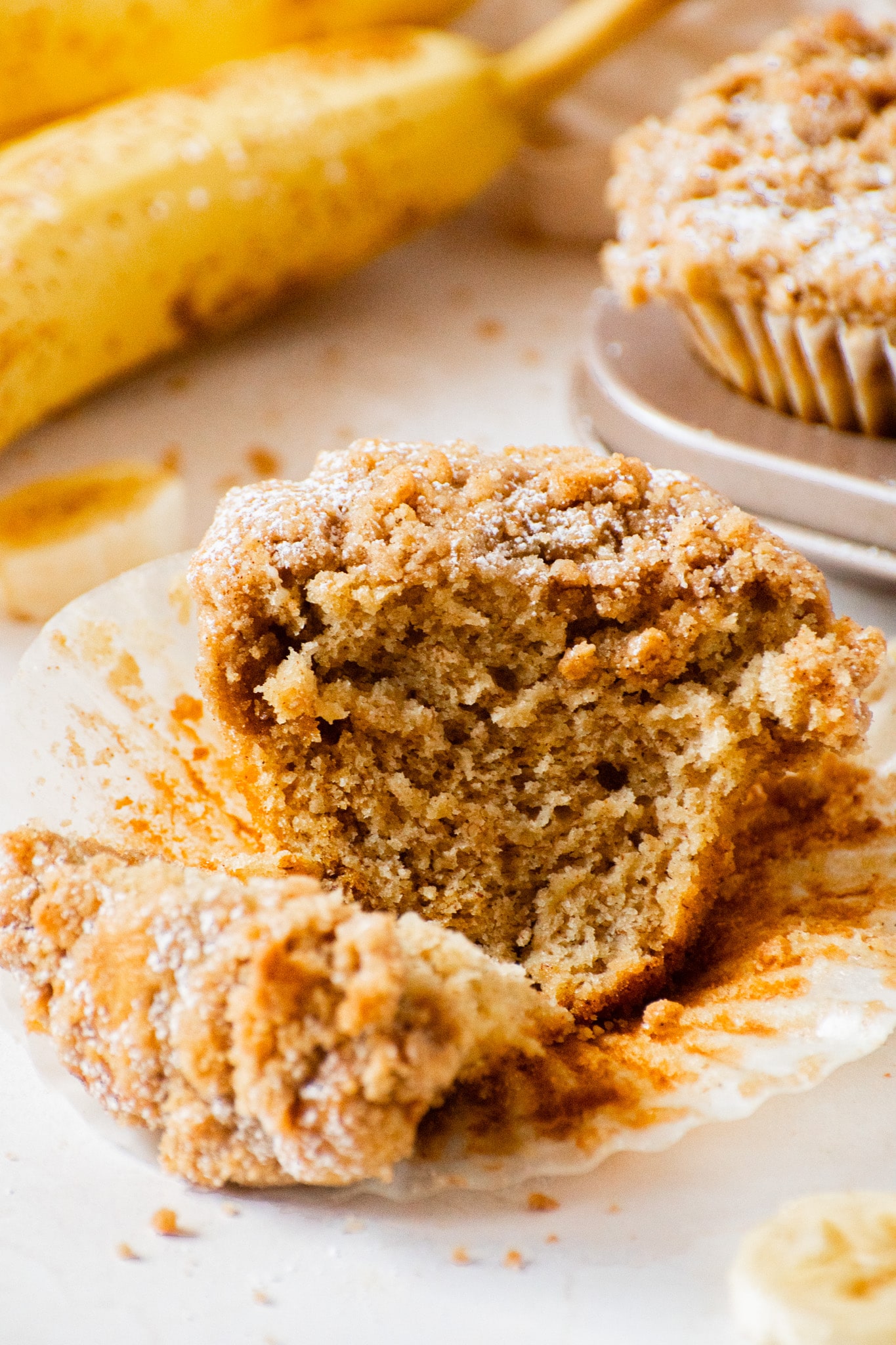 Close-up of a moist banana crumb muffin with a buttery cinnamon crumble topping, showing the soft, fluffy texture inside.