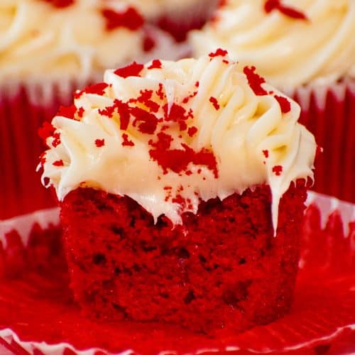 Close-up of a moist red velvet cupcake with cream cheese frosting, topped with red velvet crumbs, showcasing its soft texture and rich color.