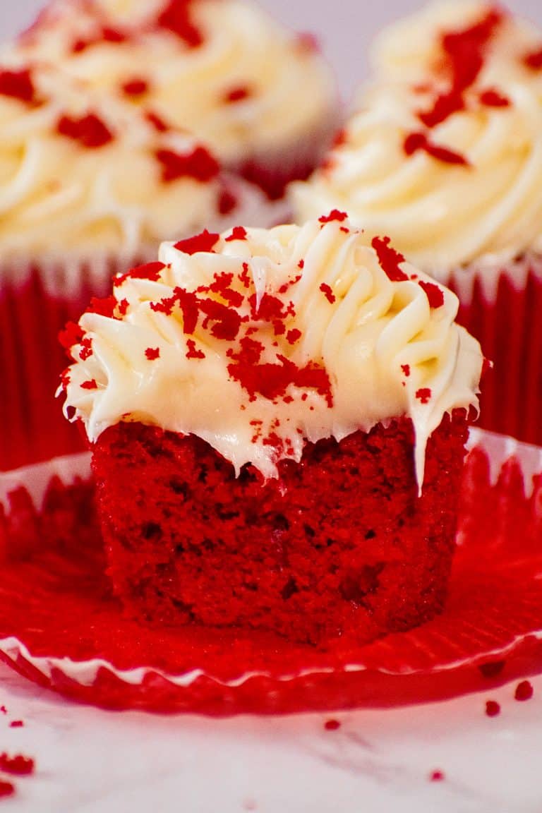 Close-up of a moist red velvet cupcake with cream cheese frosting, topped with red velvet crumbs, showcasing its soft texture and rich color.