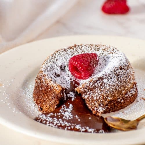 Rich and gooey molten lava cake dusted with powdered sugar, topped with a fresh raspberry, and served on a plate with a golden spoon.