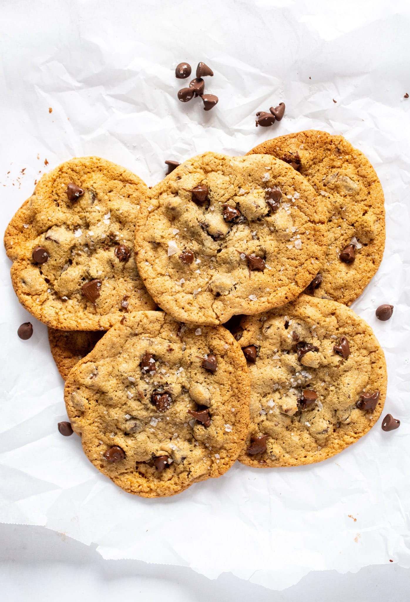 Pile of gluten free chocolate chip cookies with crisp golden edges, chewy centers, melty chocolate chips, and flaky sea salt on parchment paper