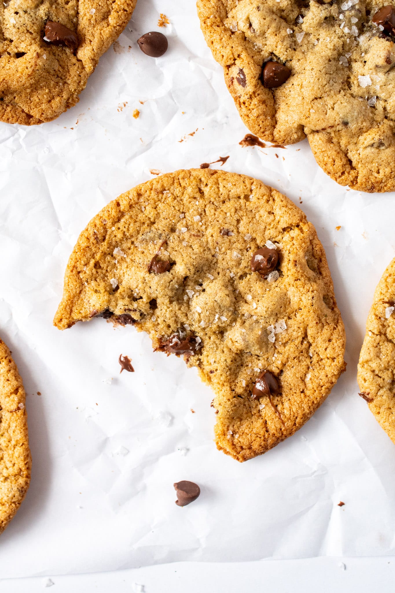 Gluten free chocolate chip cookie with crisp golden edges, chewy center, melty chocolate chips, and flaky sea salt on parchment paper