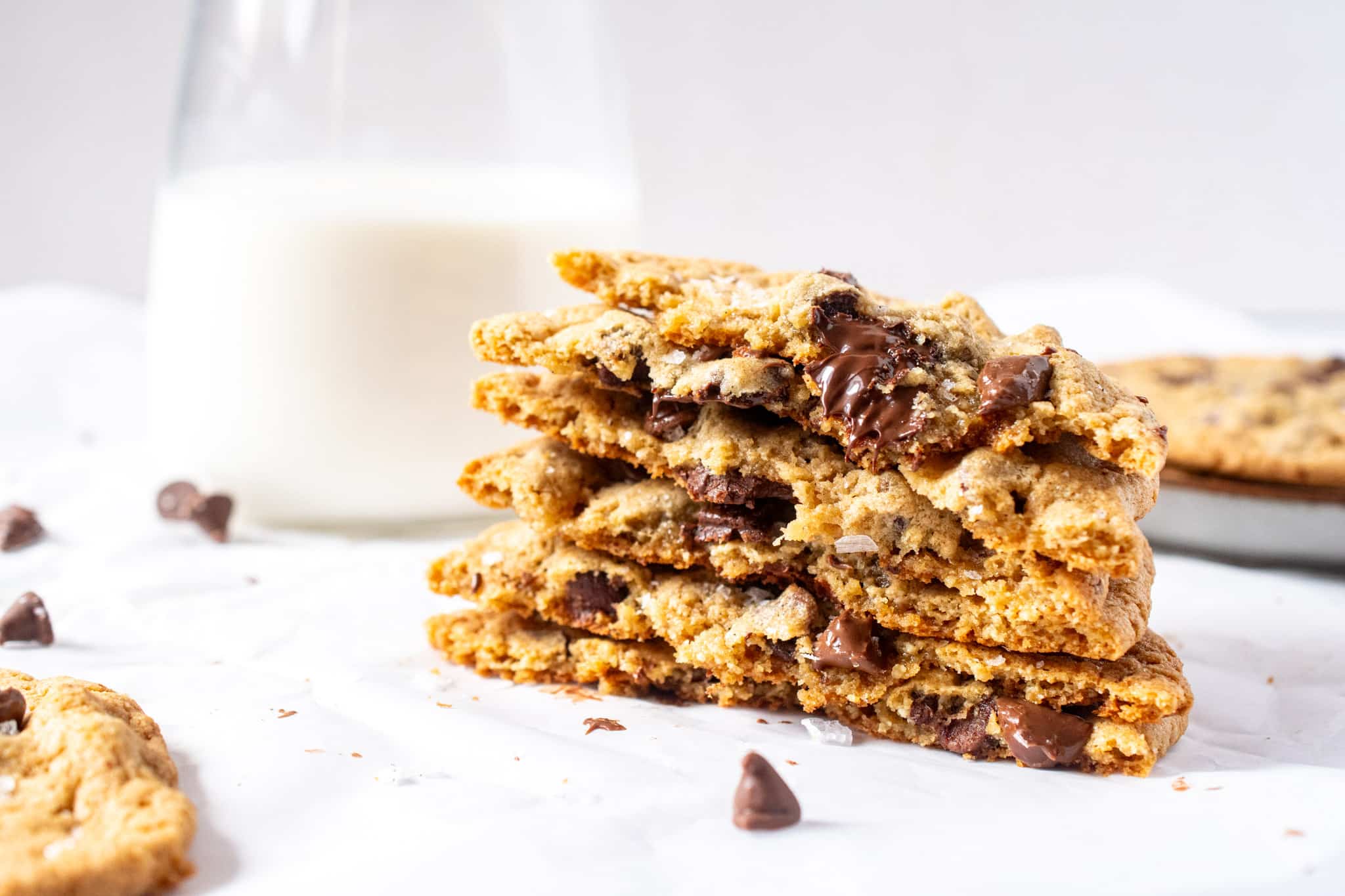 Gluten free chocolate chip cookies with crisp edges and melty chocolate, stacked with a glass of milk in the background.