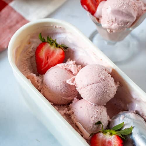 Homemade strawberry ice cream in a container with fresh strawberries and an ice cream scoop