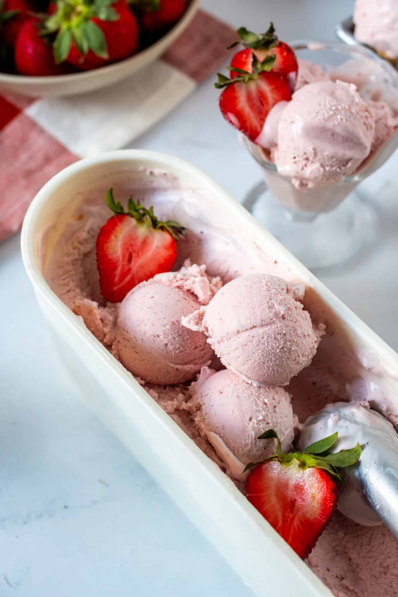 Homemade strawberry ice cream in a container with fresh strawberries and an ice cream scoop