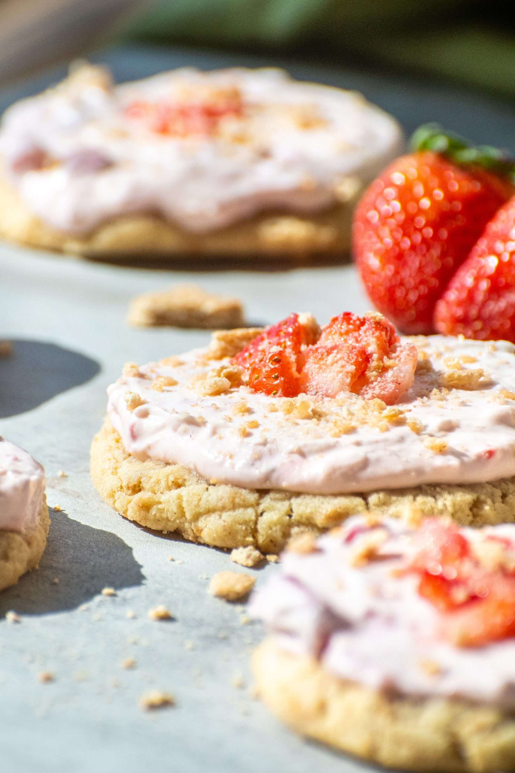 Close-up of a strawberry cheesecake cookie topped with pink cream cheese filling, sliced strawberries, and graham cracker crumbs