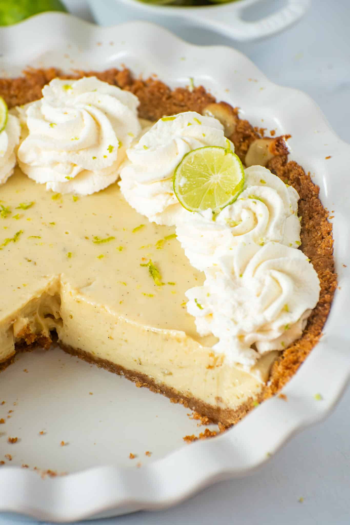 Creamy homemade Key Lime Pie with graham cracker crust, whipped cream, lime zest, and a slice removed.