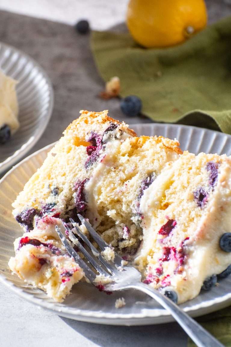 Moist lemon blueberry cake slice with cream cheese frosting on a plate and fork