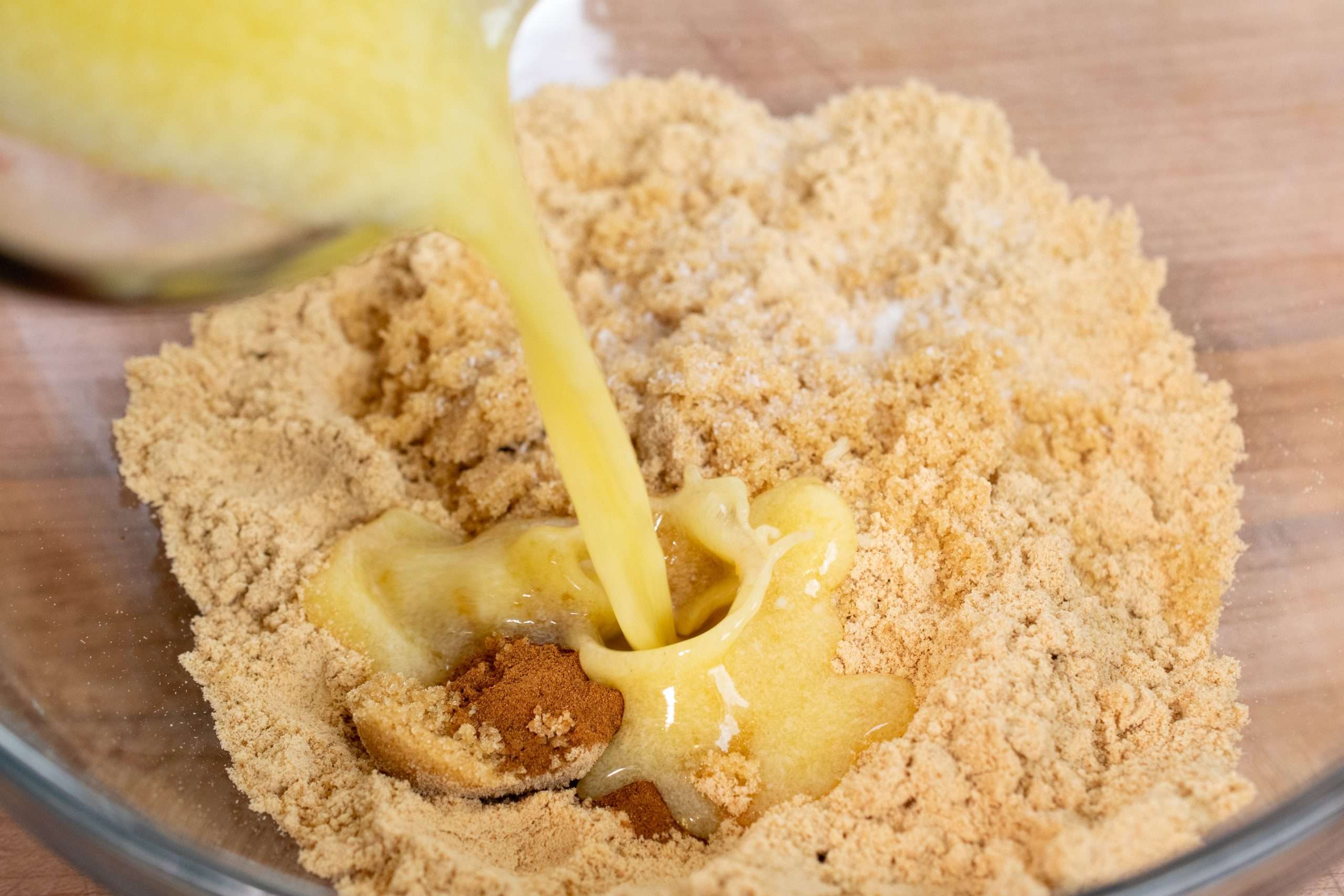 Pouring melted butter into graham cracker crumbs to make cheesecake crust