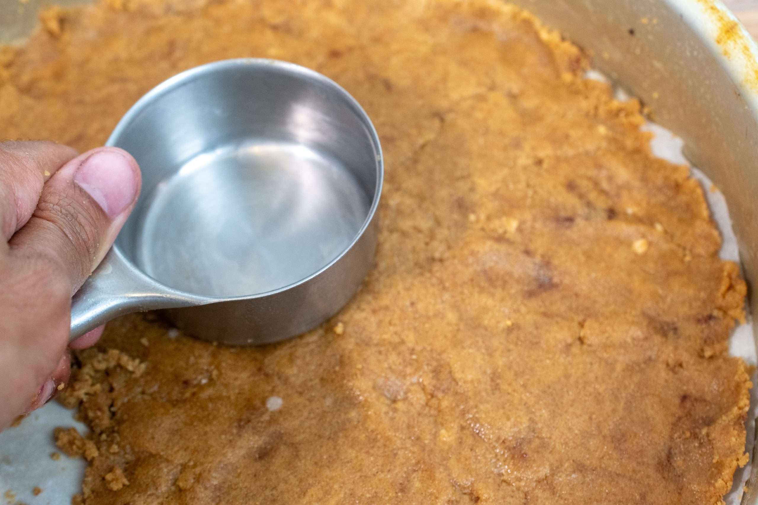 Pressing graham cracker crust into a springform pan using a measuring cup