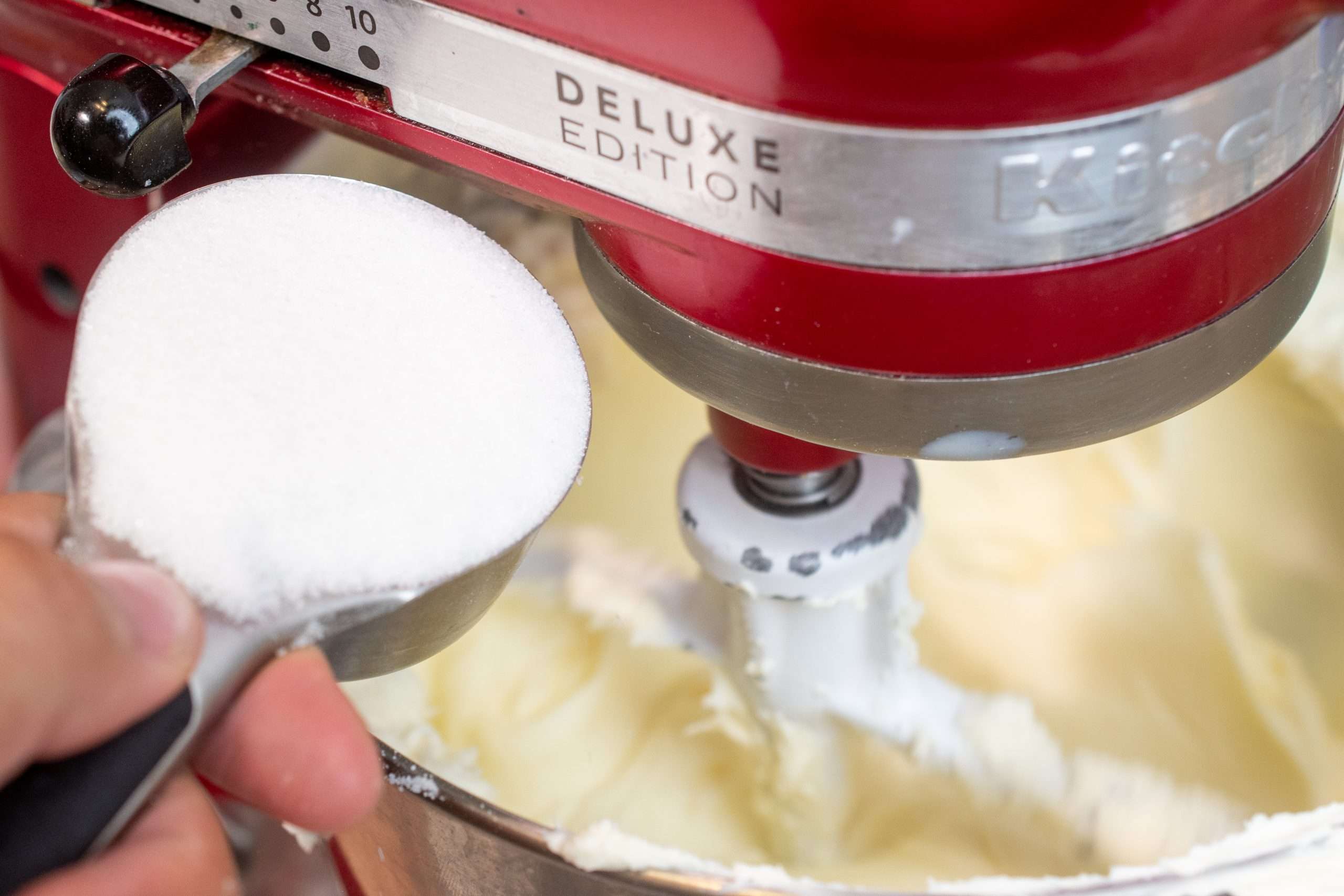 Pouring sugar into the cheesecake batter in a stand mixer bowl