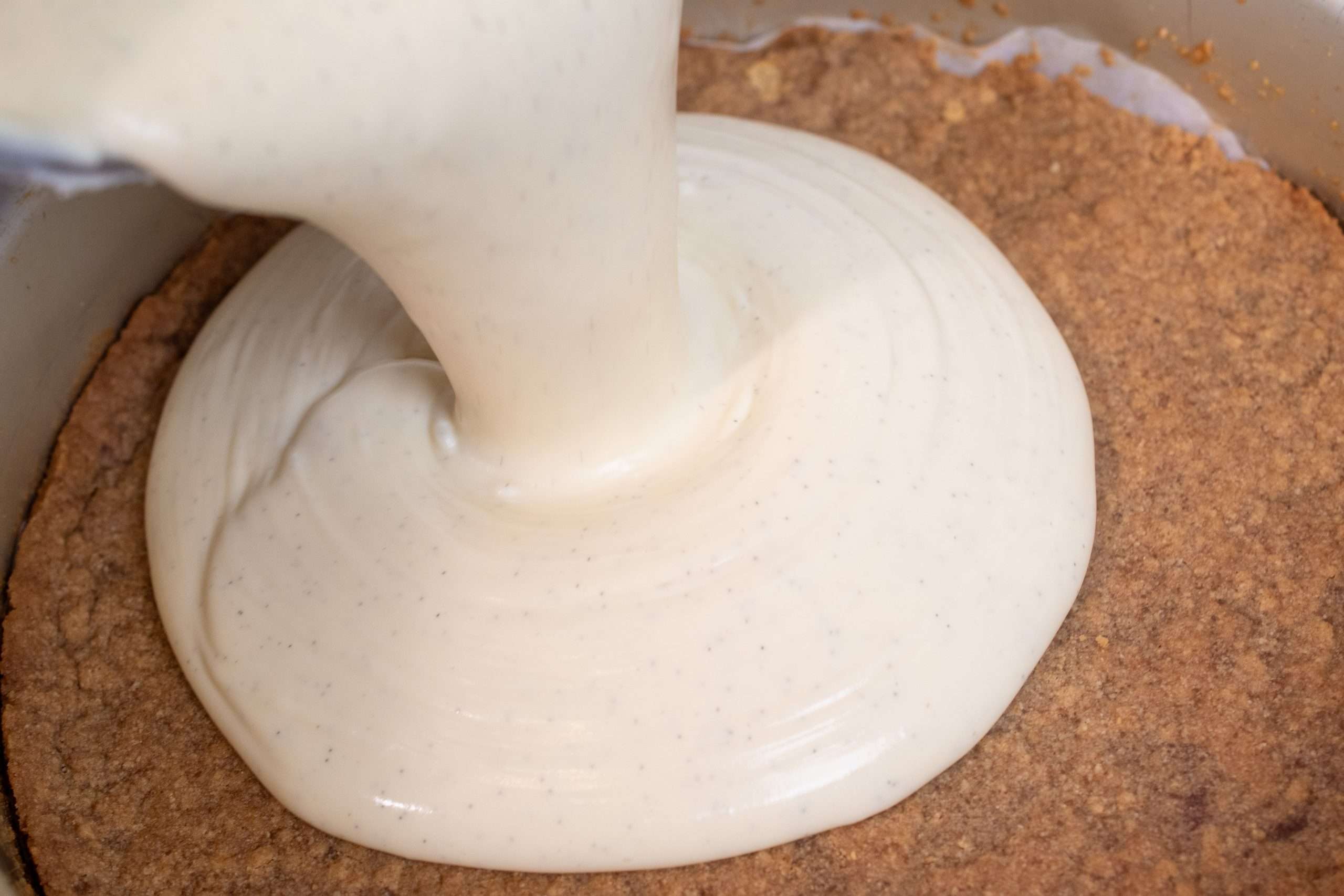 Pouring vanilla cheesecake batter into graham cracker crust