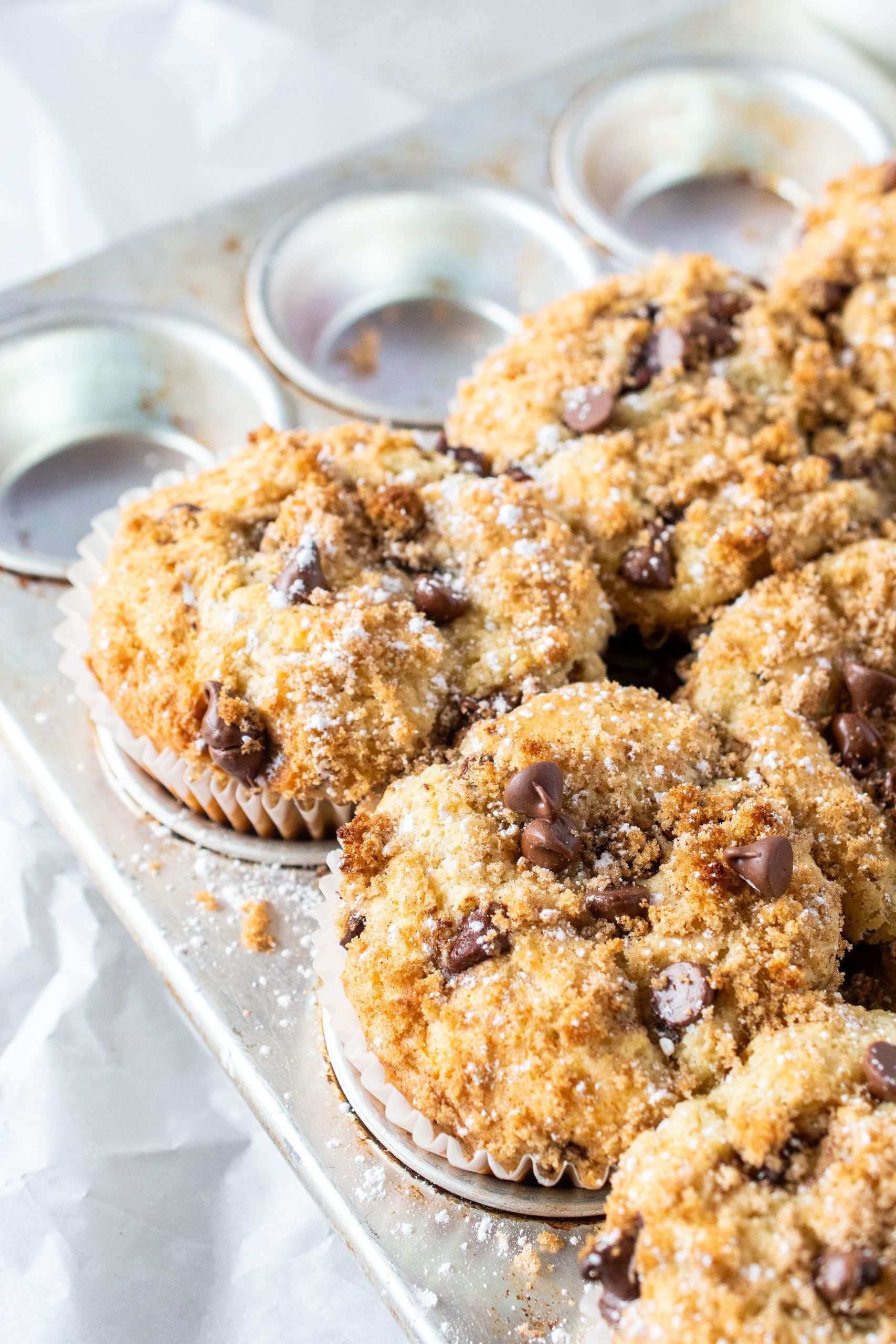 Freshly baked chocolate chip muffins in a muffin pan topped with cinnamon sugar and melted chocolate chips.