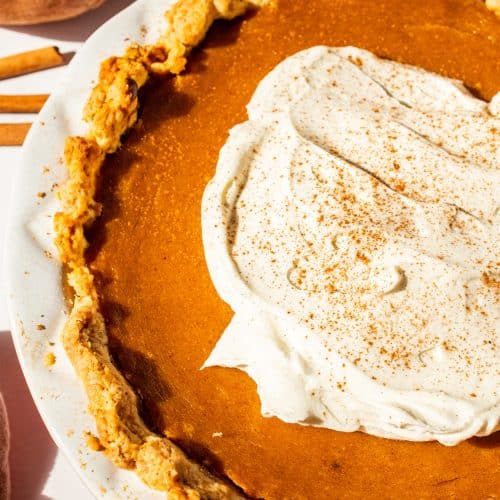 Overhead shot of a homemade sweet potato pie topped with whipped cream and sprinkled with cinnamon. The golden, flaky crust surrounds a silky orange filling — the perfect Southern dessert for Thanksgiving or any cozy fall gathering.