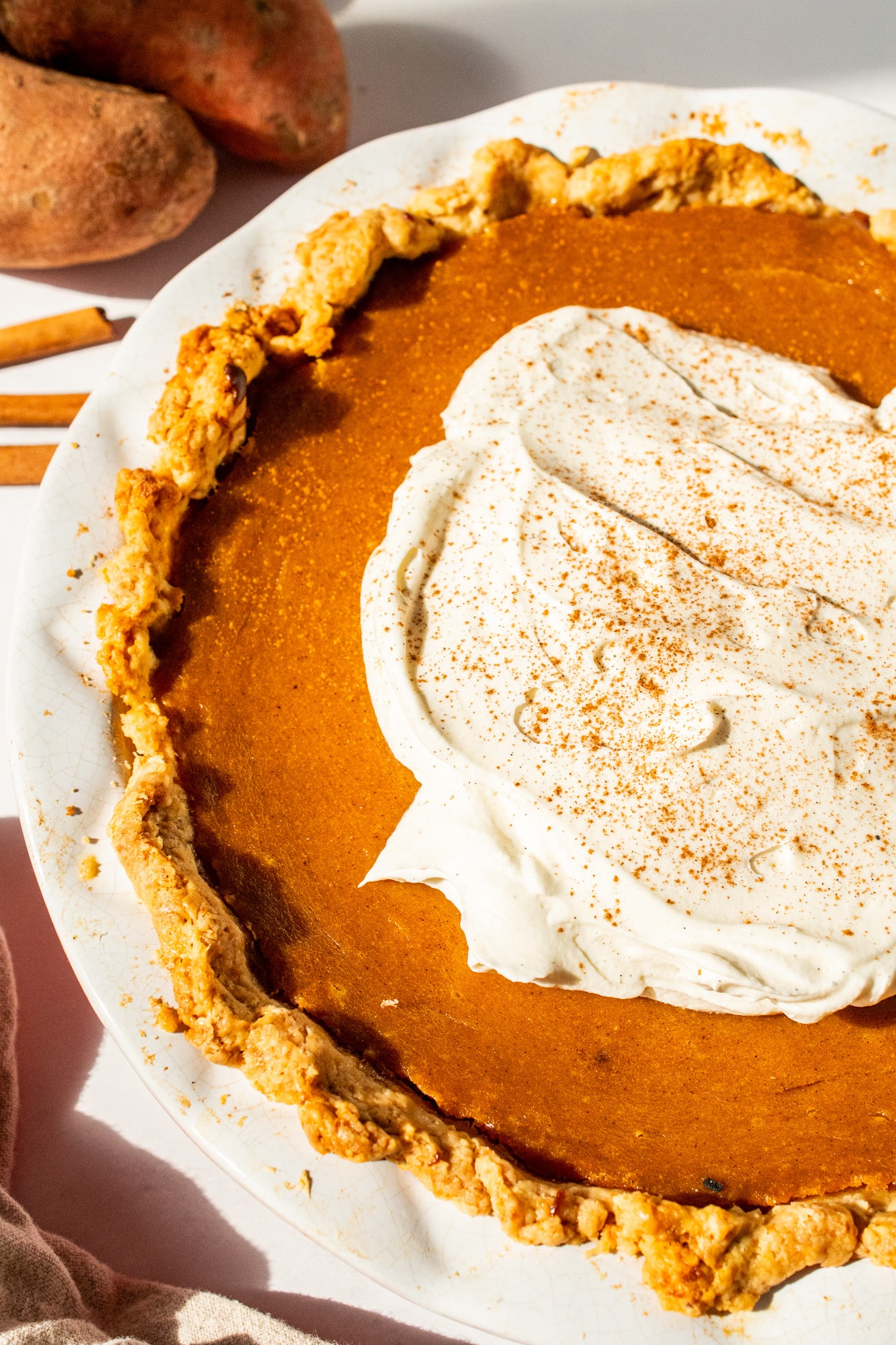 Overhead shot of a homemade sweet potato pie topped with whipped cream and sprinkled with cinnamon. The golden, flaky crust surrounds a silky orange filling — the perfect Southern dessert for Thanksgiving or any cozy fall gathering.