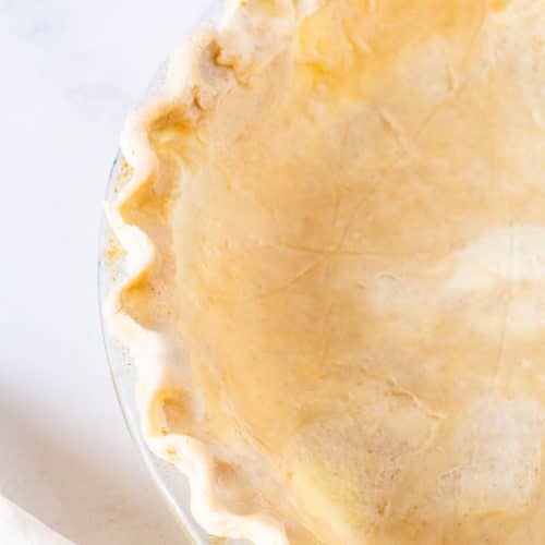 Unbaked all butter flaky pie crust in a glass pie dish, ready to be filled and baked for the perfect golden homemade pie.