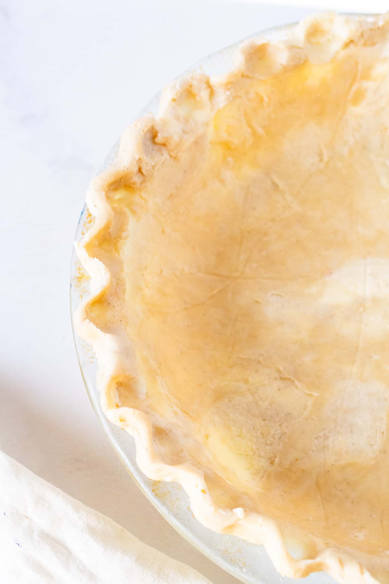 Unbaked all butter flaky pie crust in a glass pie dish, ready to be filled and baked for the perfect golden homemade pie.