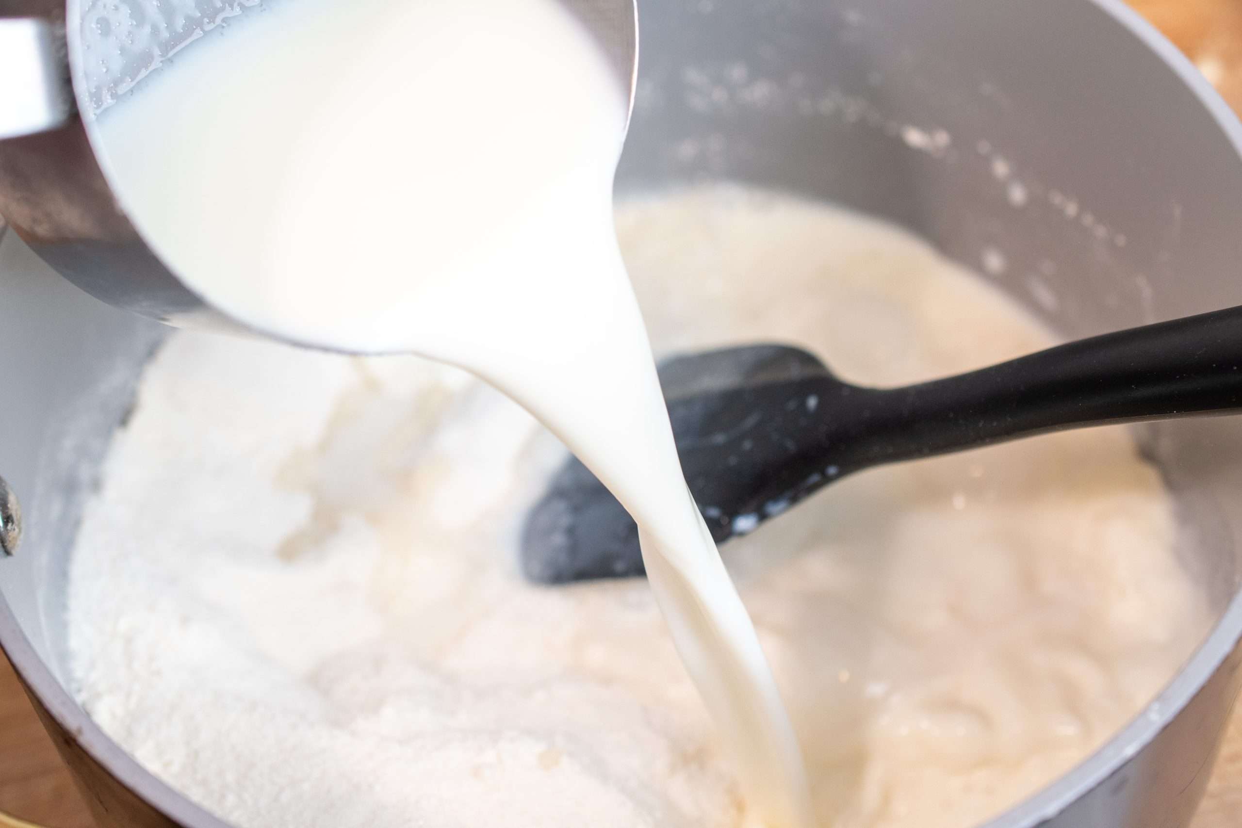 Pouring milk into dry ingredients to create a smooth mixture.