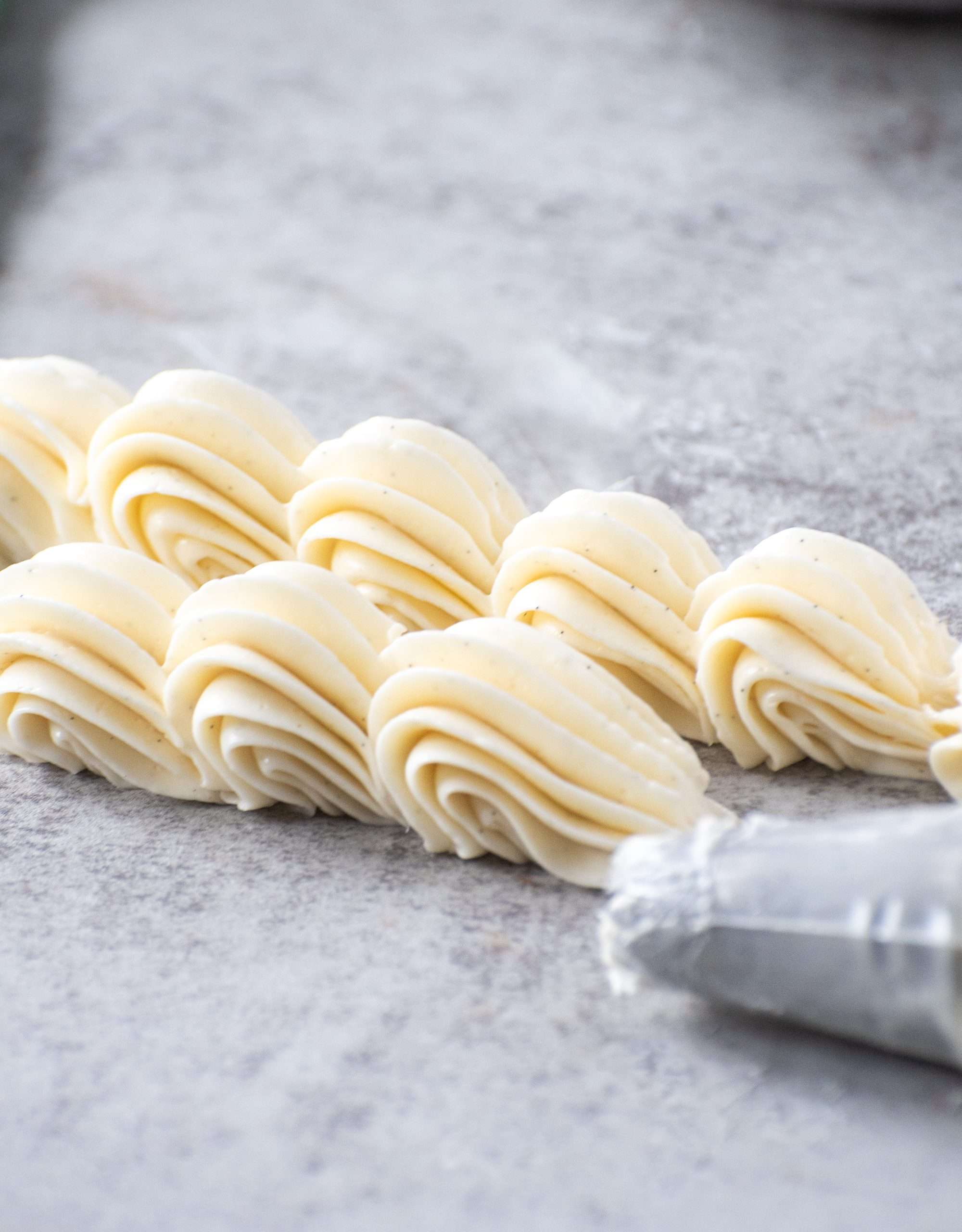 Piped vegan buttercream rosettes made with ermine frosting, shown on a grey surface.