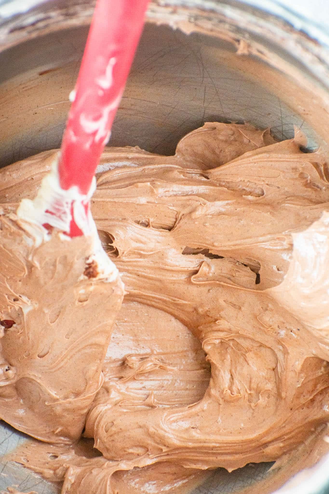 Close-up of creamy vegan chocolate frosting with a red spatula folding the mixture.