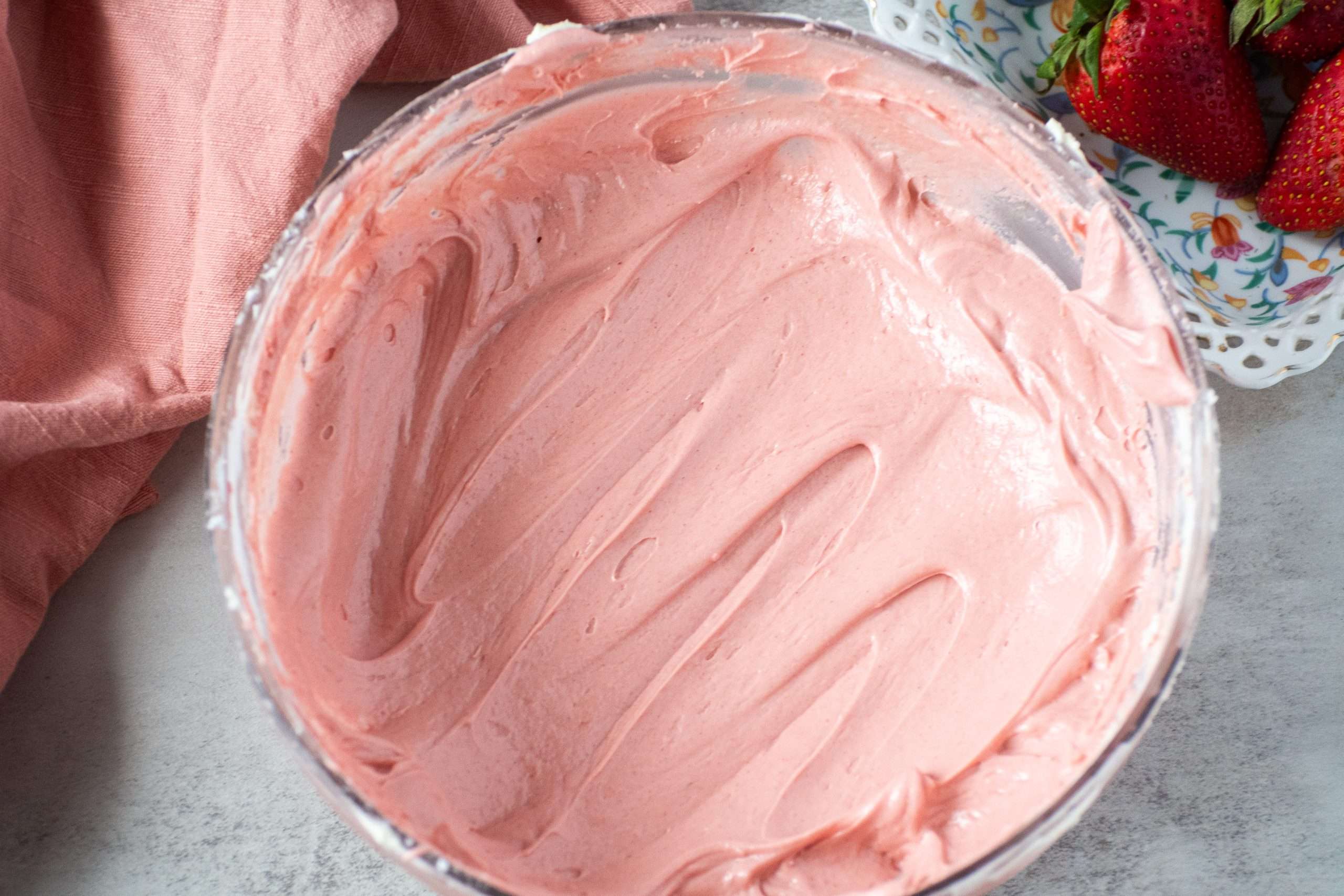 Fluffy strawberry cream cheese frosting in a glass mixing bowl, swirled smooth and ready to use.