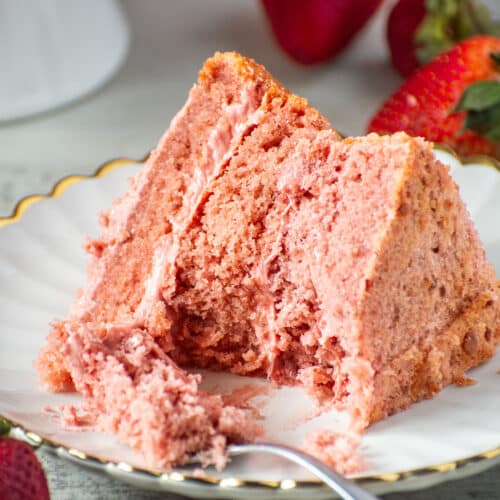 Slice of moist strawberry cake from scratch on a white scalloped plate with fresh strawberries and a fork.