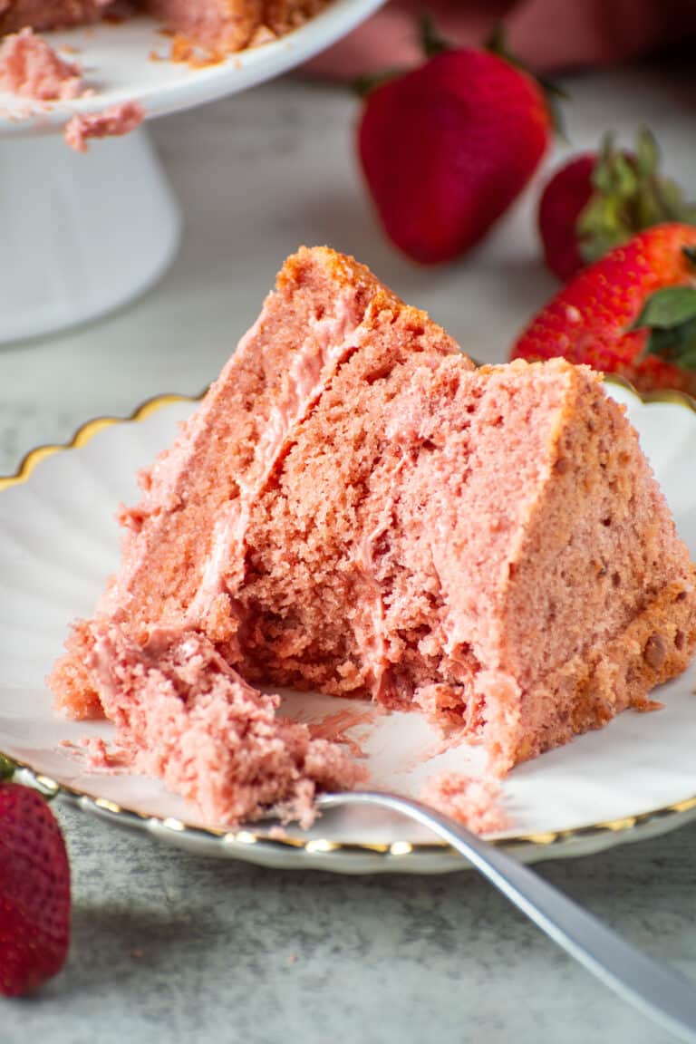 Slice of moist strawberry cake from scratch on a white scalloped plate with fresh strawberries and a fork.