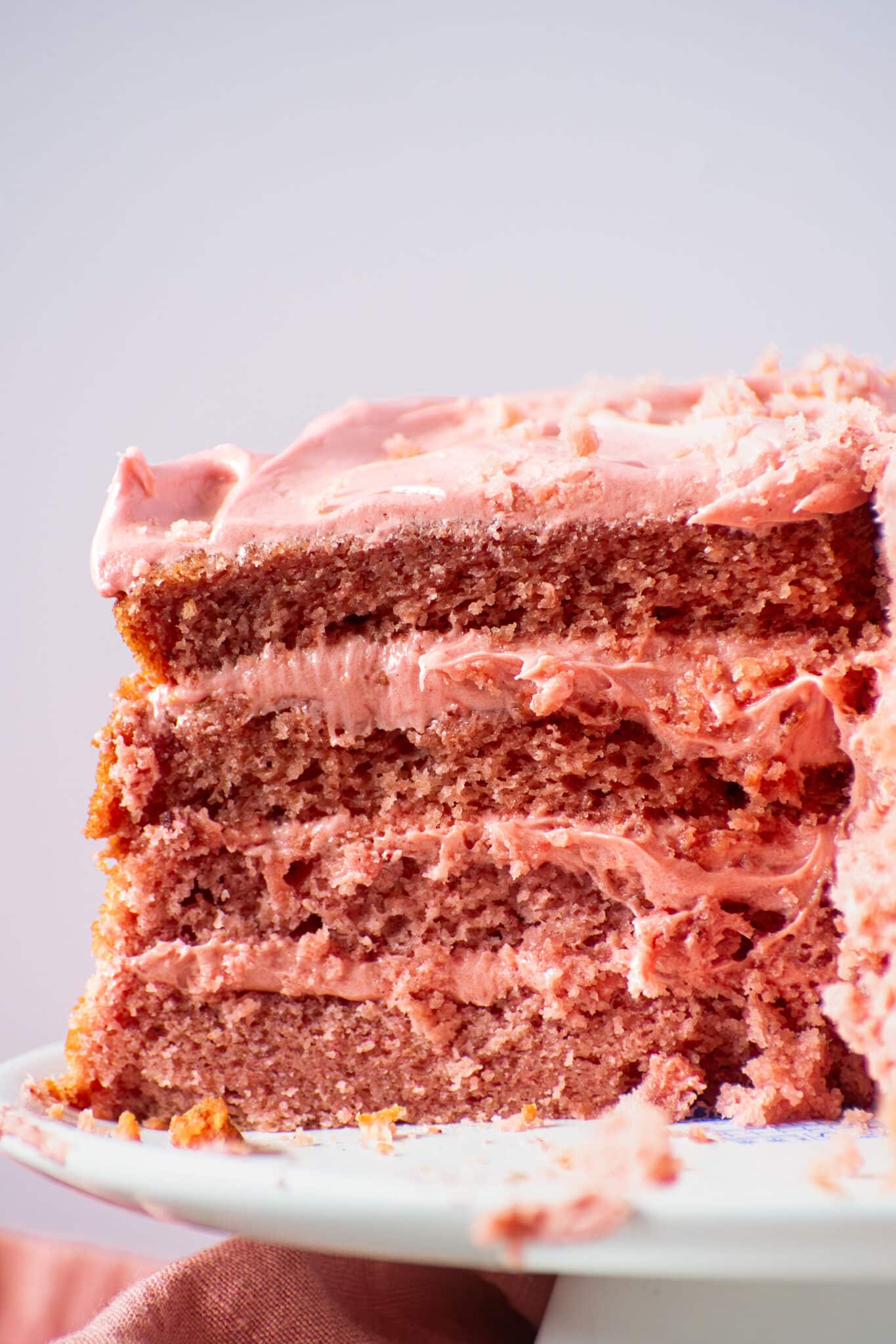 Close-up of three moist strawberry cake layers with strawberry buttercream frosting between each layer.
