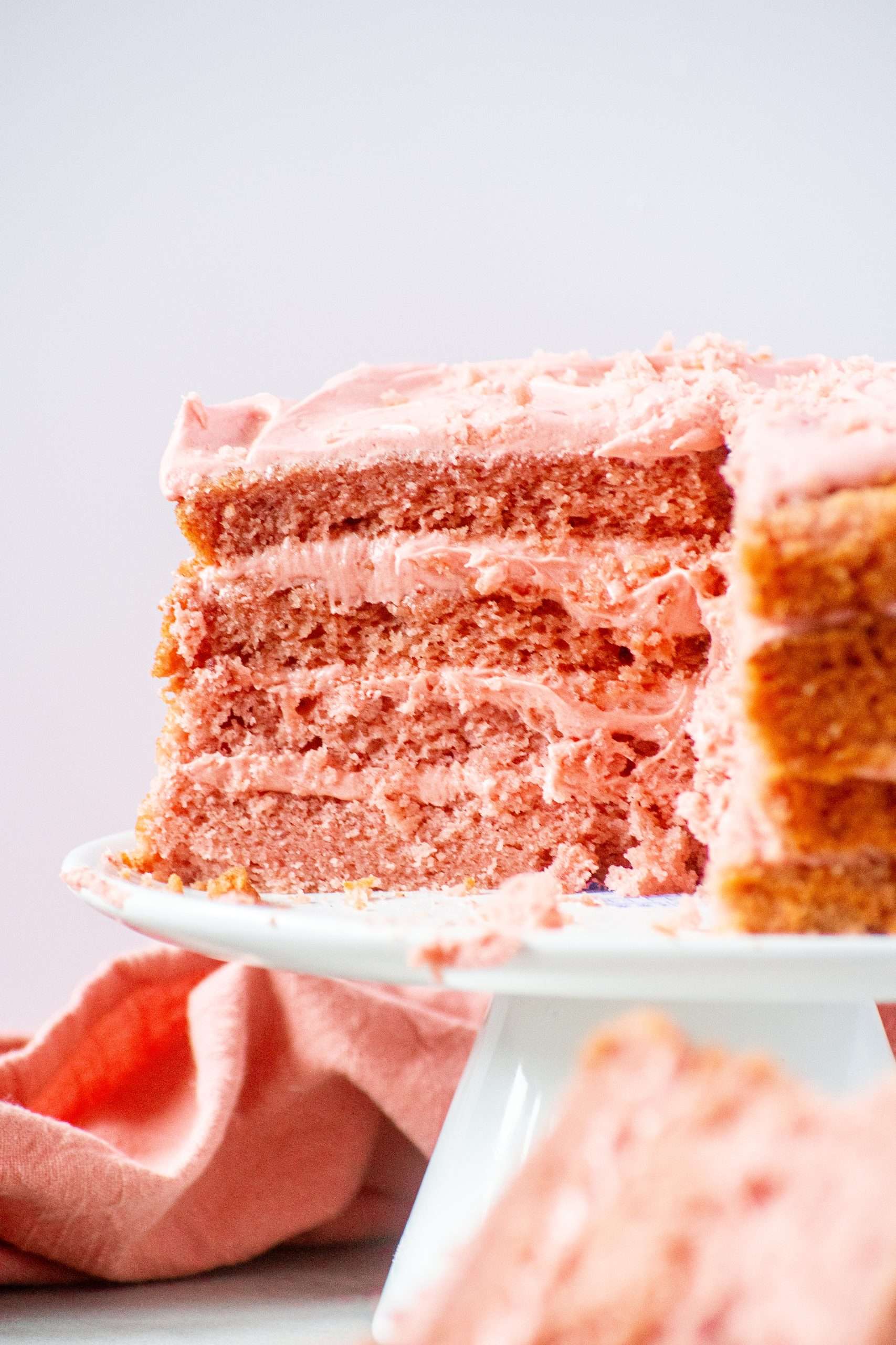 Three-layer strawberry cake with strawberry cream cheese frosting, sliced to show fluffy texture and rich pink layers.