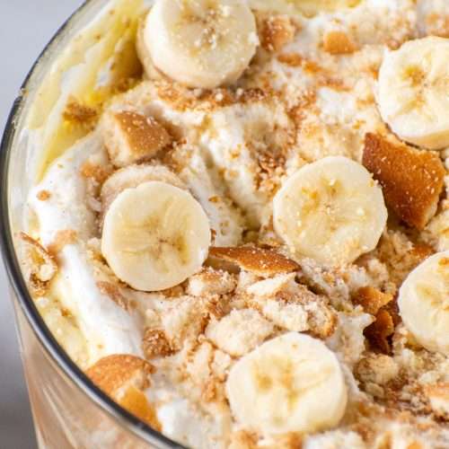 Close-up of homemade banana pudding topped with fresh banana slices, crushed Nilla wafers, and whipped cream in a glass dish.