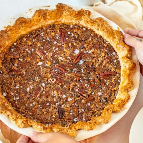 Hands holding a whole brown butter pecan pie with flaky golden crust
