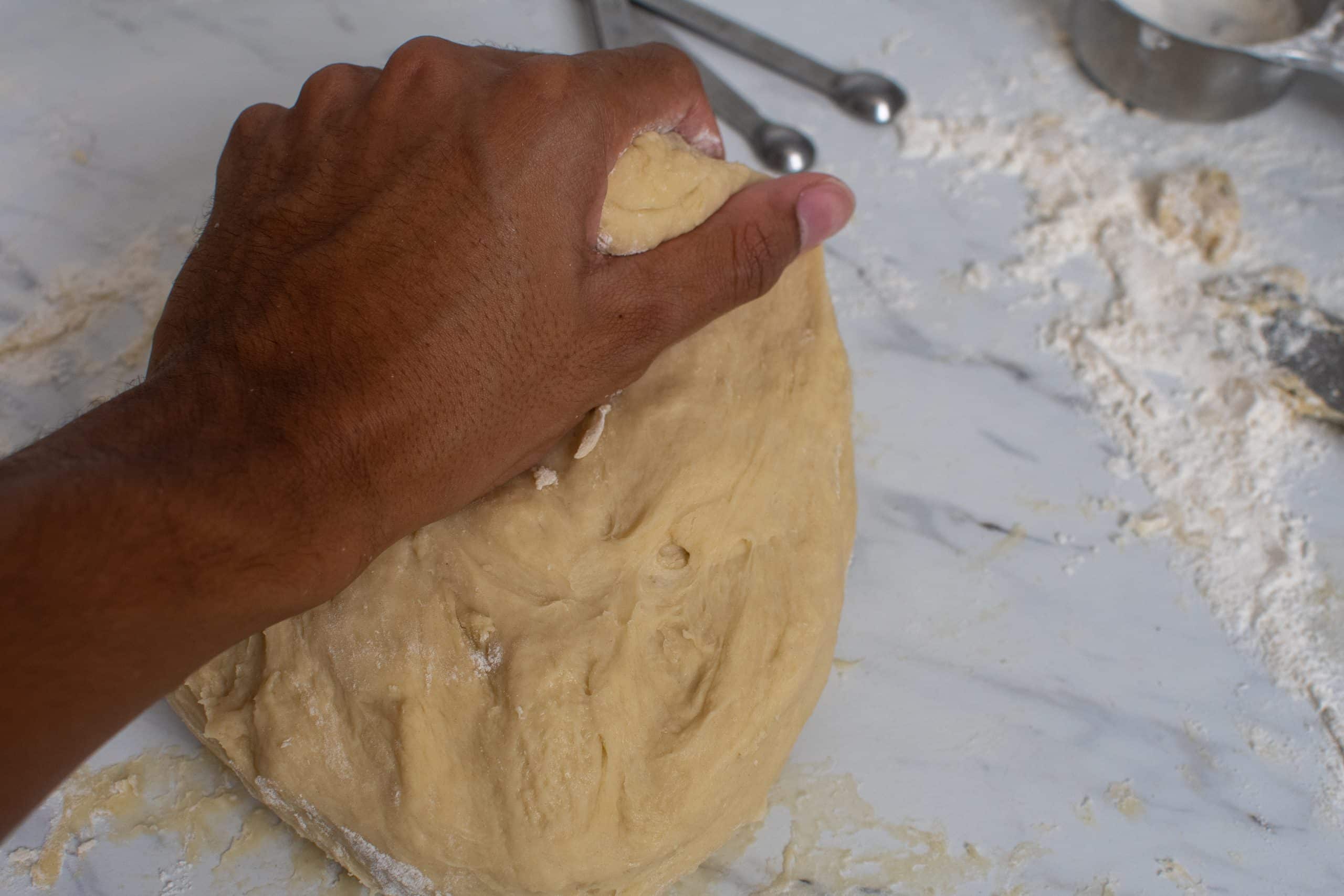Hand kneading soft dough on a lightly floured surface.