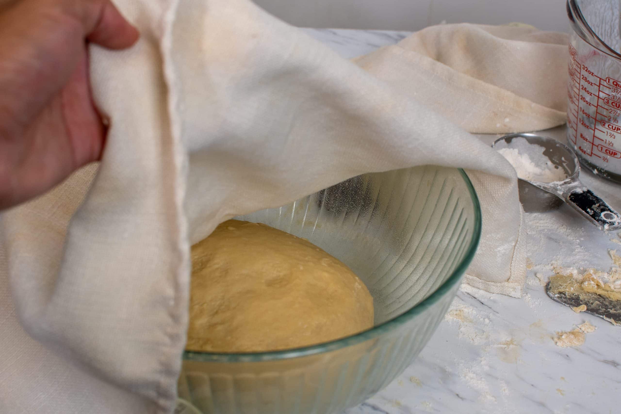 Soft dough rising in a greased bowl covered with a towel.