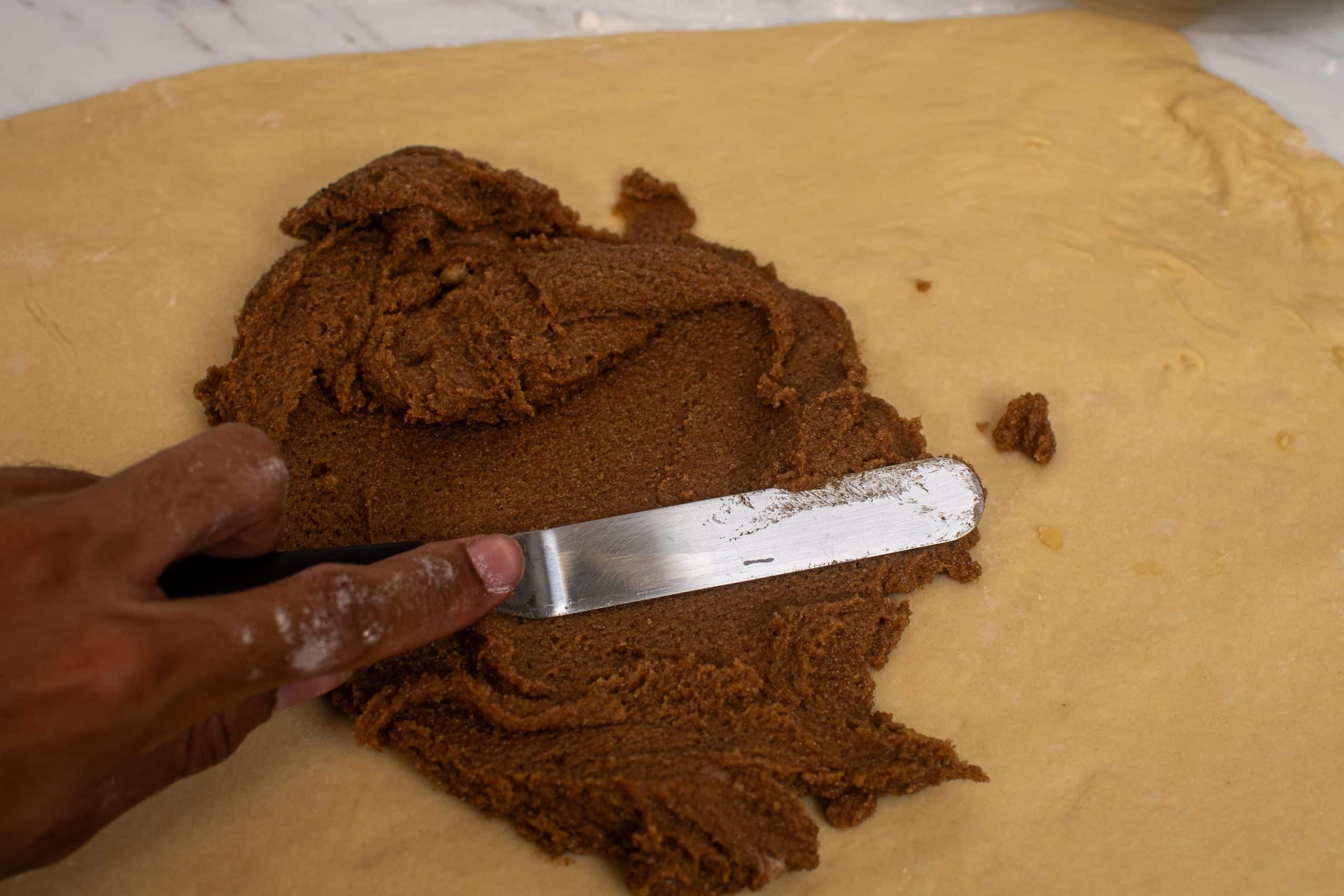 Spreading cinnamon sugar filling evenly on rolled-out dough.