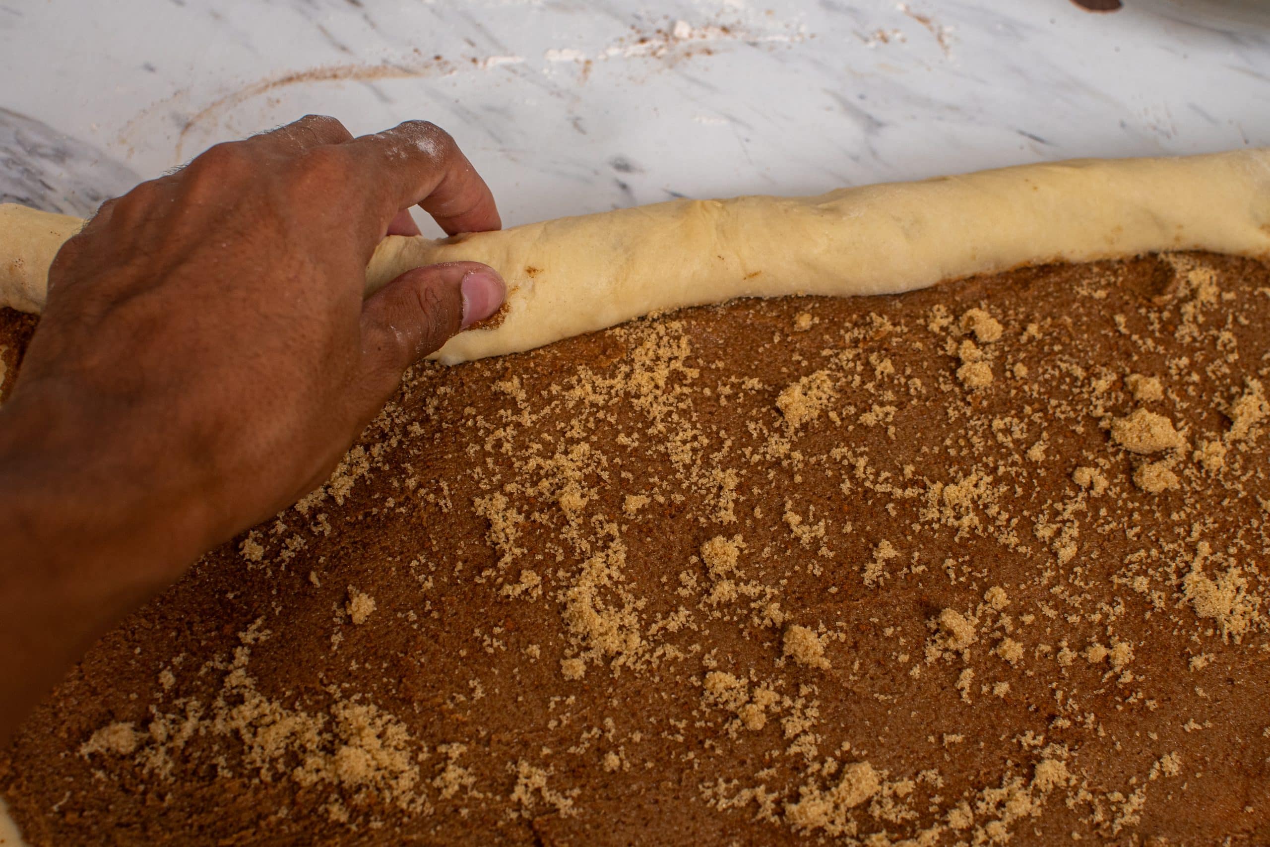 Rolling the dough tightly into a log to shape the rolls.