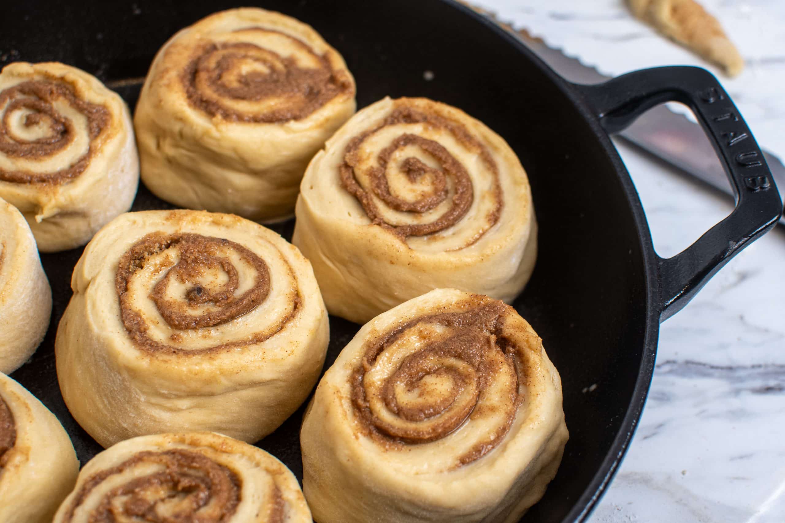 Unbaked make-ahead cinnamon rolls proofed in a cast iron skillet, ready to bake in the morning.