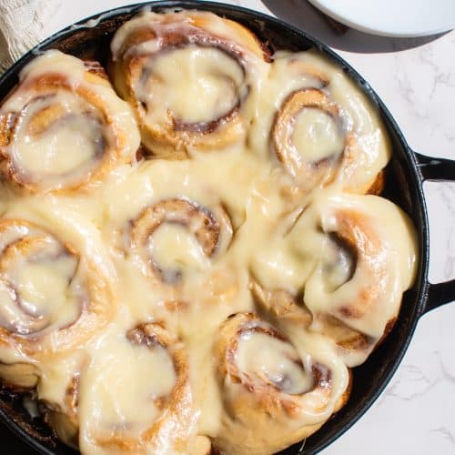 Cinnamon rolls topped with cream cheese icing in a cast iron skillet.